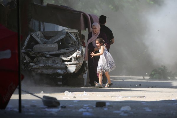 TOPSHOT - A Palestinian mother and her daughter rush for cover during an Israeli strike in the Al-Bureij camp in the central Gaza Strip on July 4, 2025. (Photo by Eyad BABA / AFP)